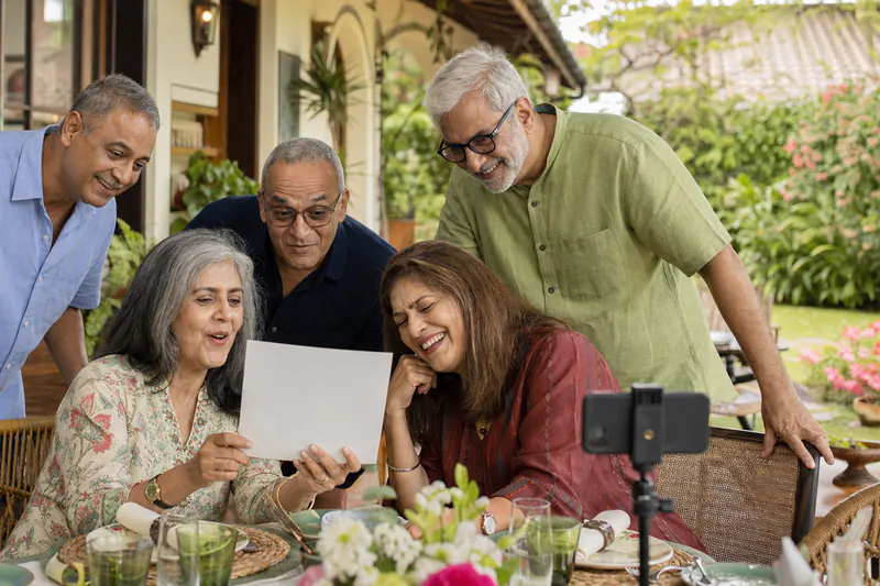 Mature Indian friends laughing together as they revisit an old photograph at a reunion