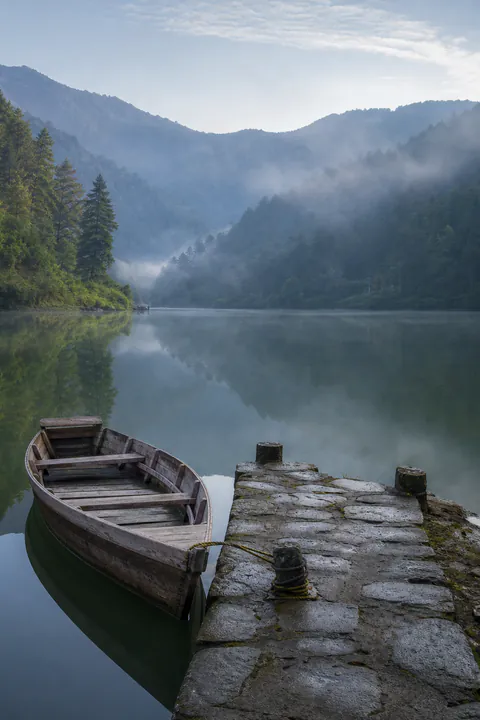 A rowboat tied beside a quiet misty mountain lake in Kumaon
